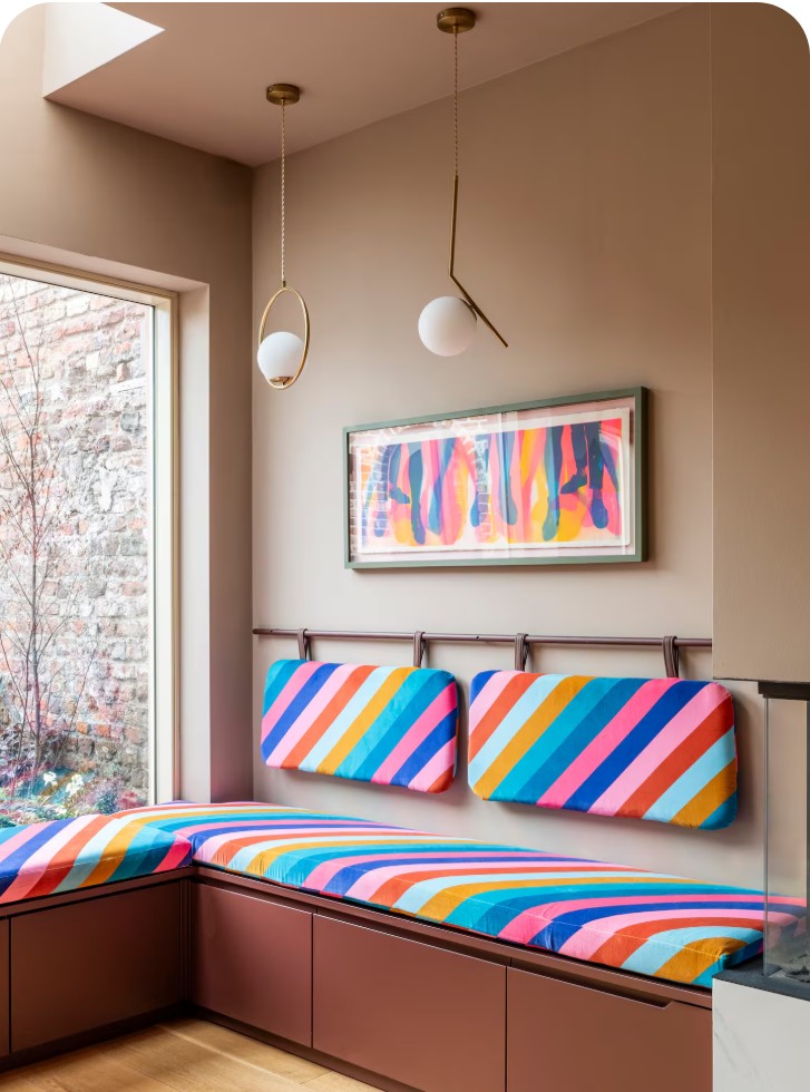 Window banquette with rainbow-striped cushions under brass pendant lights