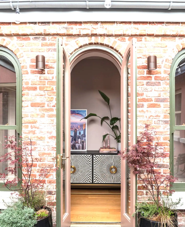 Three green-framed arches in the brick courtyard, with pink doors open onto the house