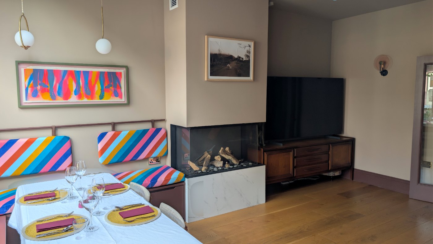 Living room with the table set for dinner beside the striped banquette, the fireplace and a framed print