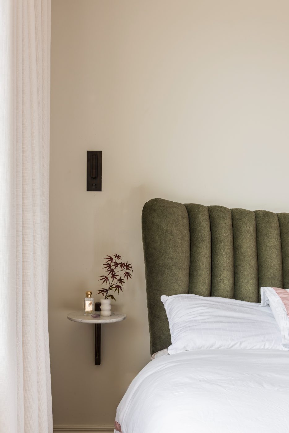 Bed with an olive ribbed headboard and wall light